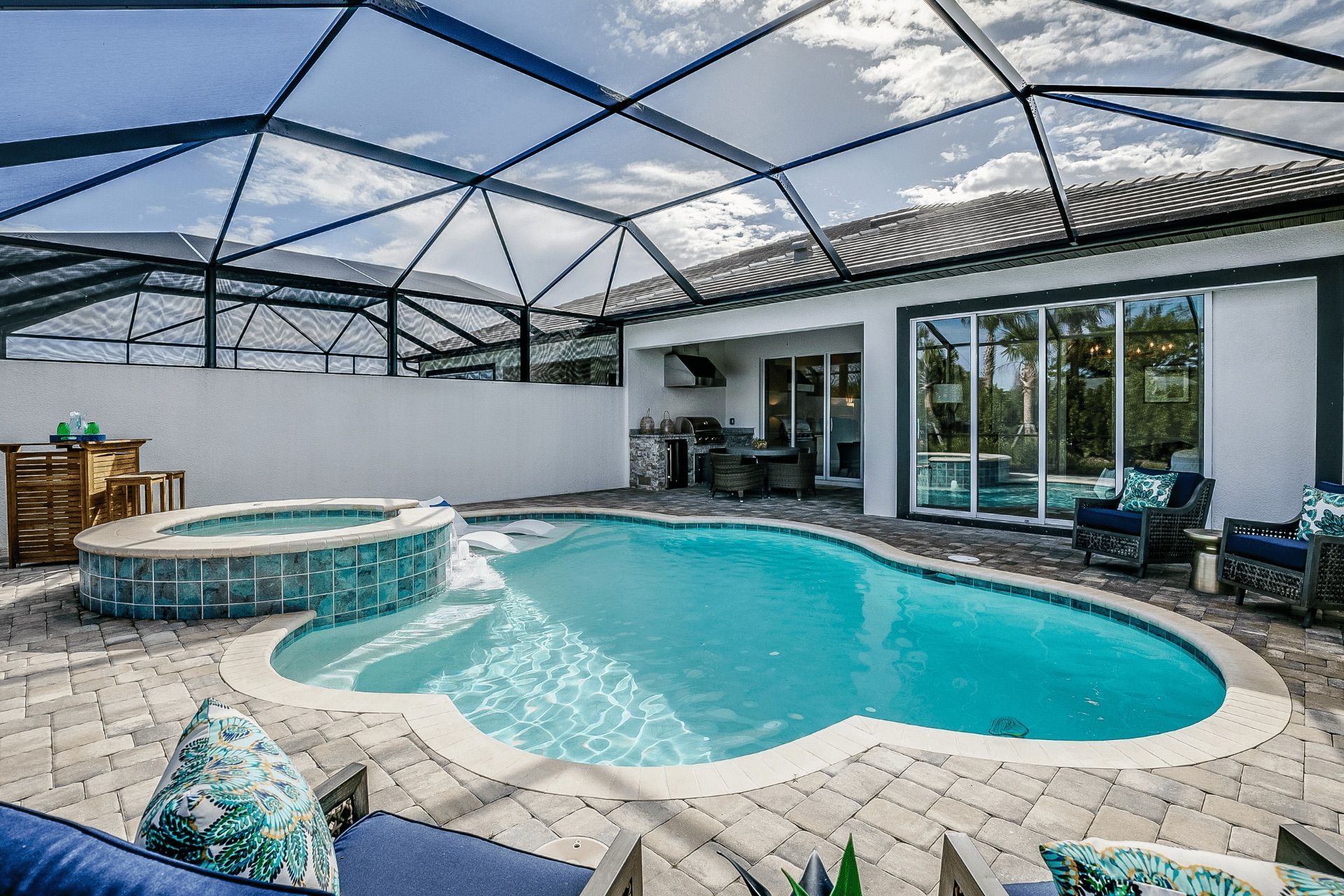 Enclosed backyard pool and spa with blue water, screened roof, and patio seating.