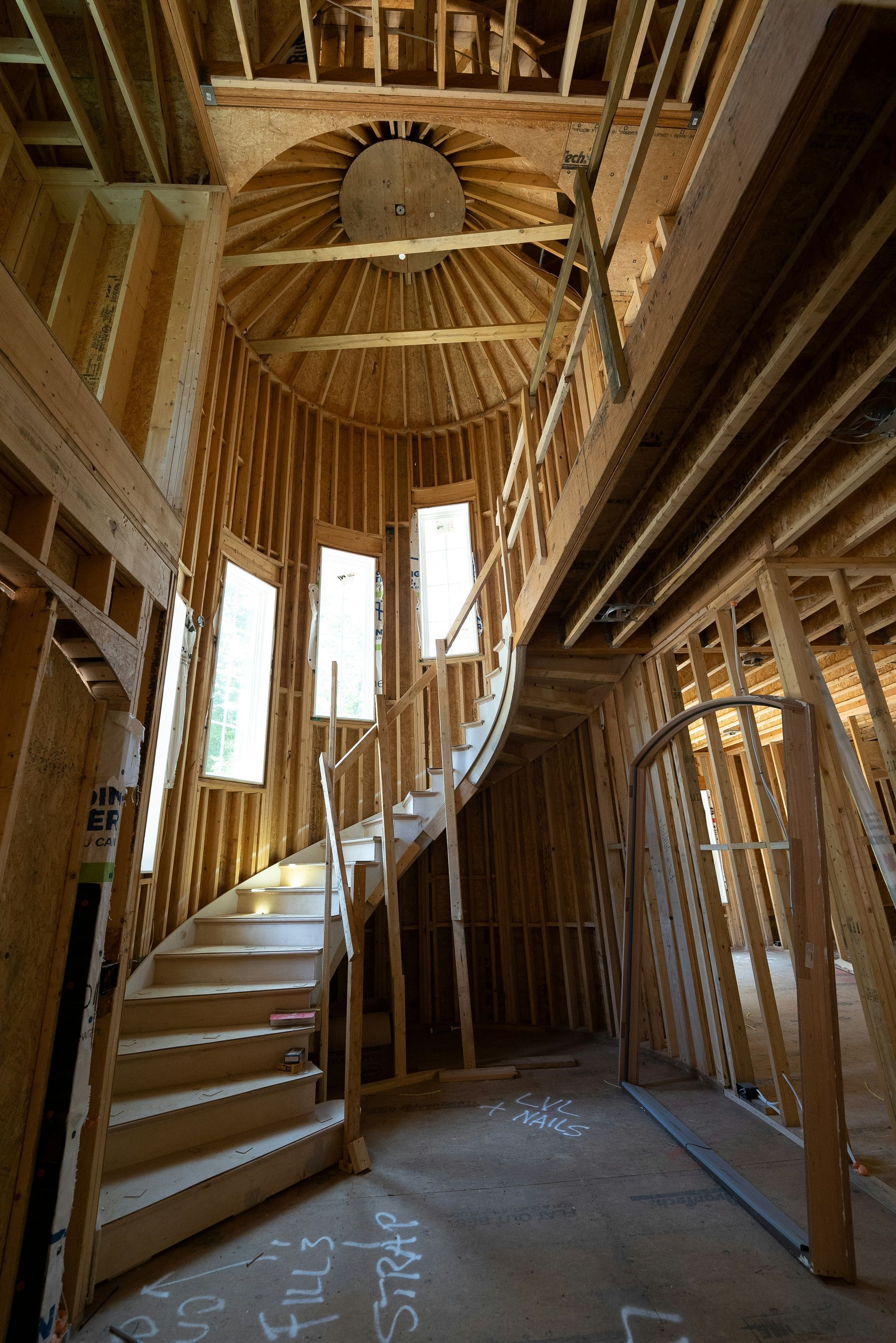 Curved wooden staircase inside a framed house under construction, with exposed beams and unfinished walls