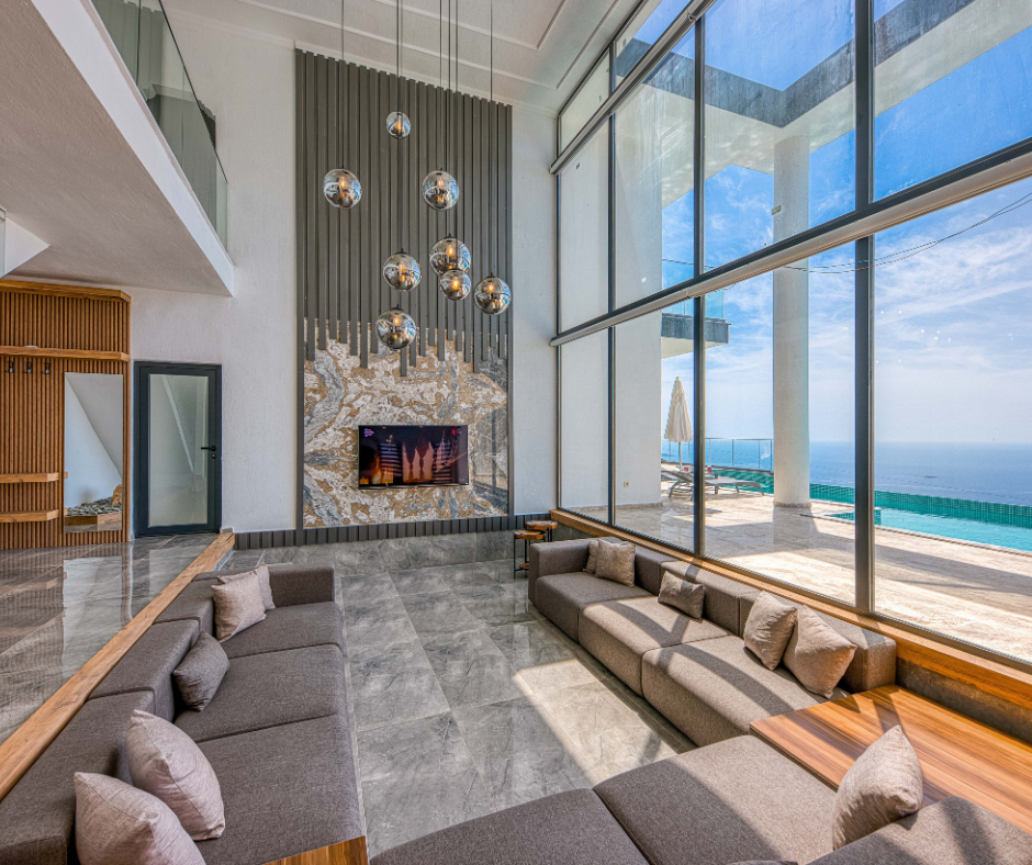Modern oceanfront living room with floor-to-ceiling windows, gray sectional seating, and a fireplace overlooking the beach