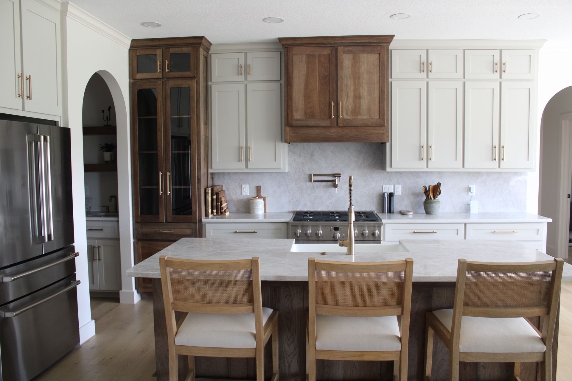 Modern white kitchen with dark refrigerator, wooden cabinets, and three bar stools at island