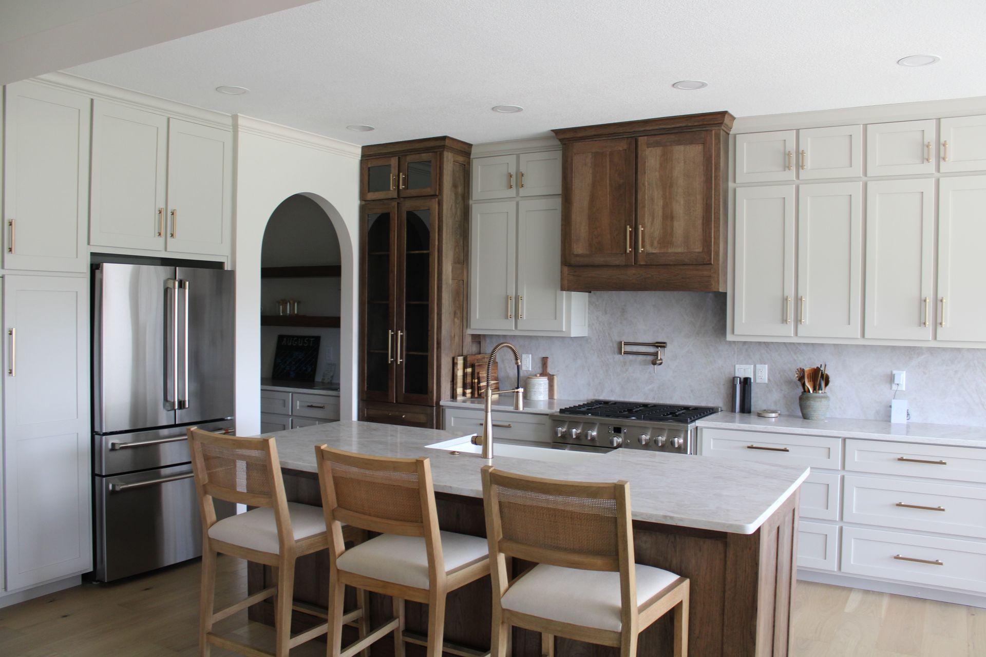 Bright modern kitchen with white cabinets, stainless fridge, island, and four wooden bar stools