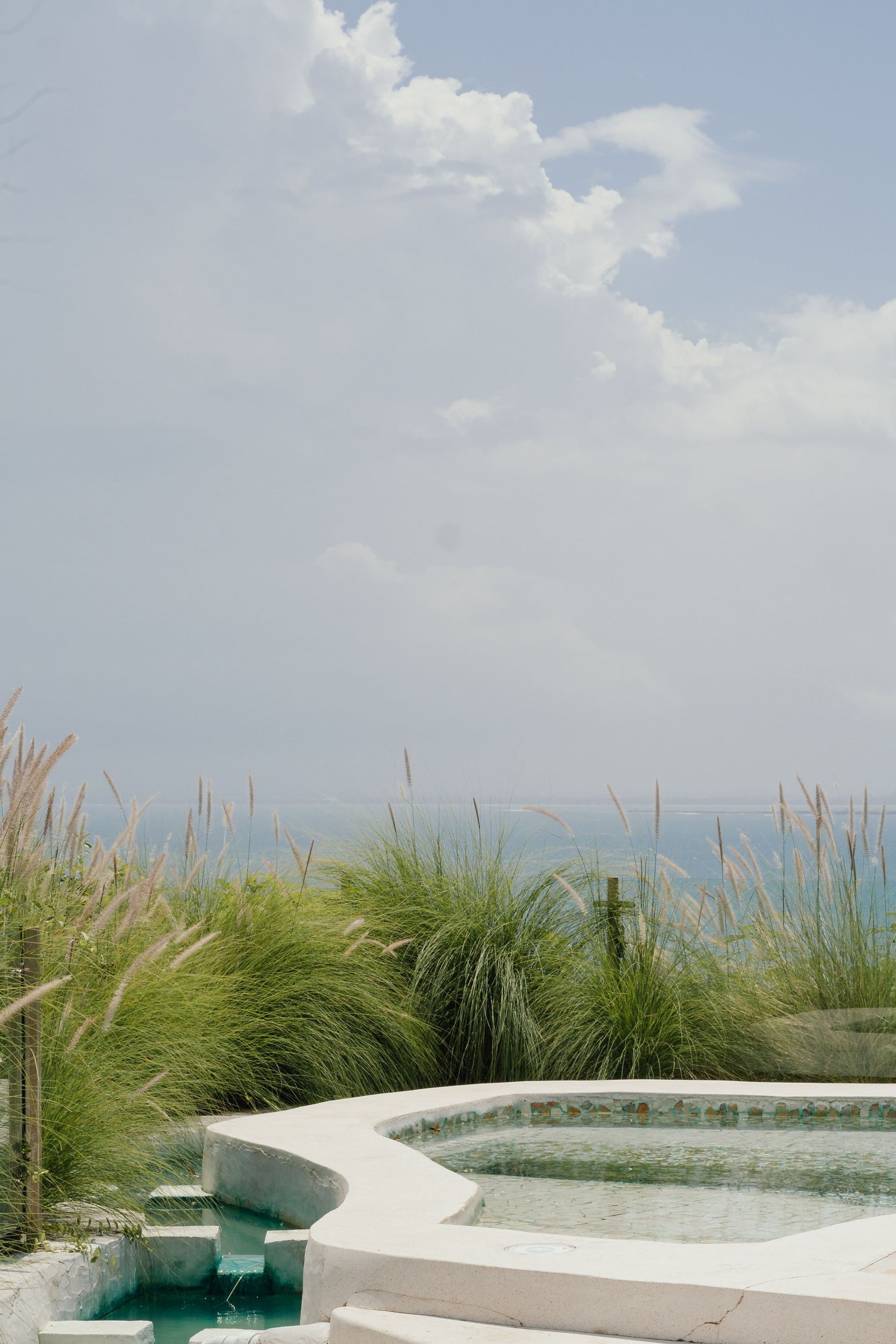 Ocean-view pool with lush grasses and a cloudy sky