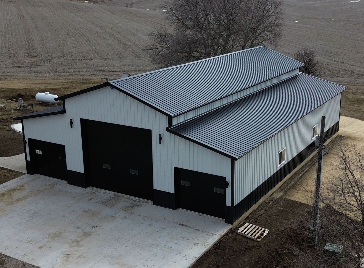 A white and black metal agricultural building with a corrugated metal roof, on a concrete pad.