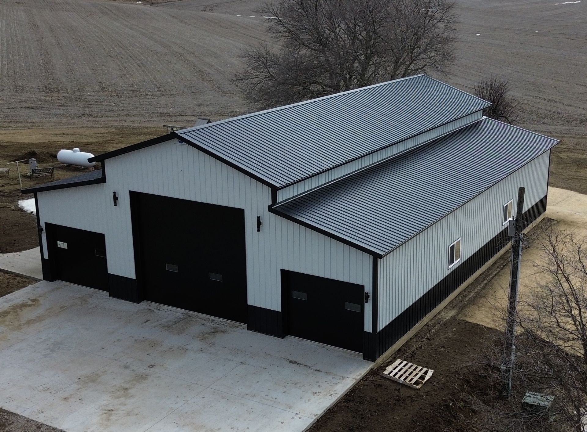 A white and black metal agricultural building with a corrugated metal roof, on a concrete pad.