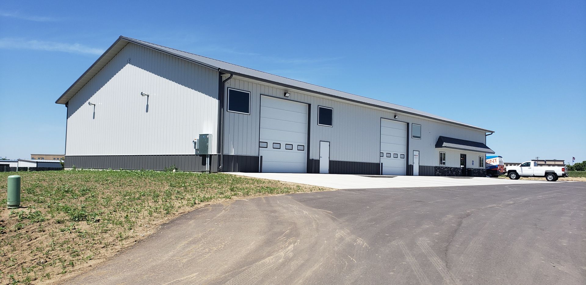 A long metal industrial building with three garage doors, a white truck parked nearby, and clear blue sky.