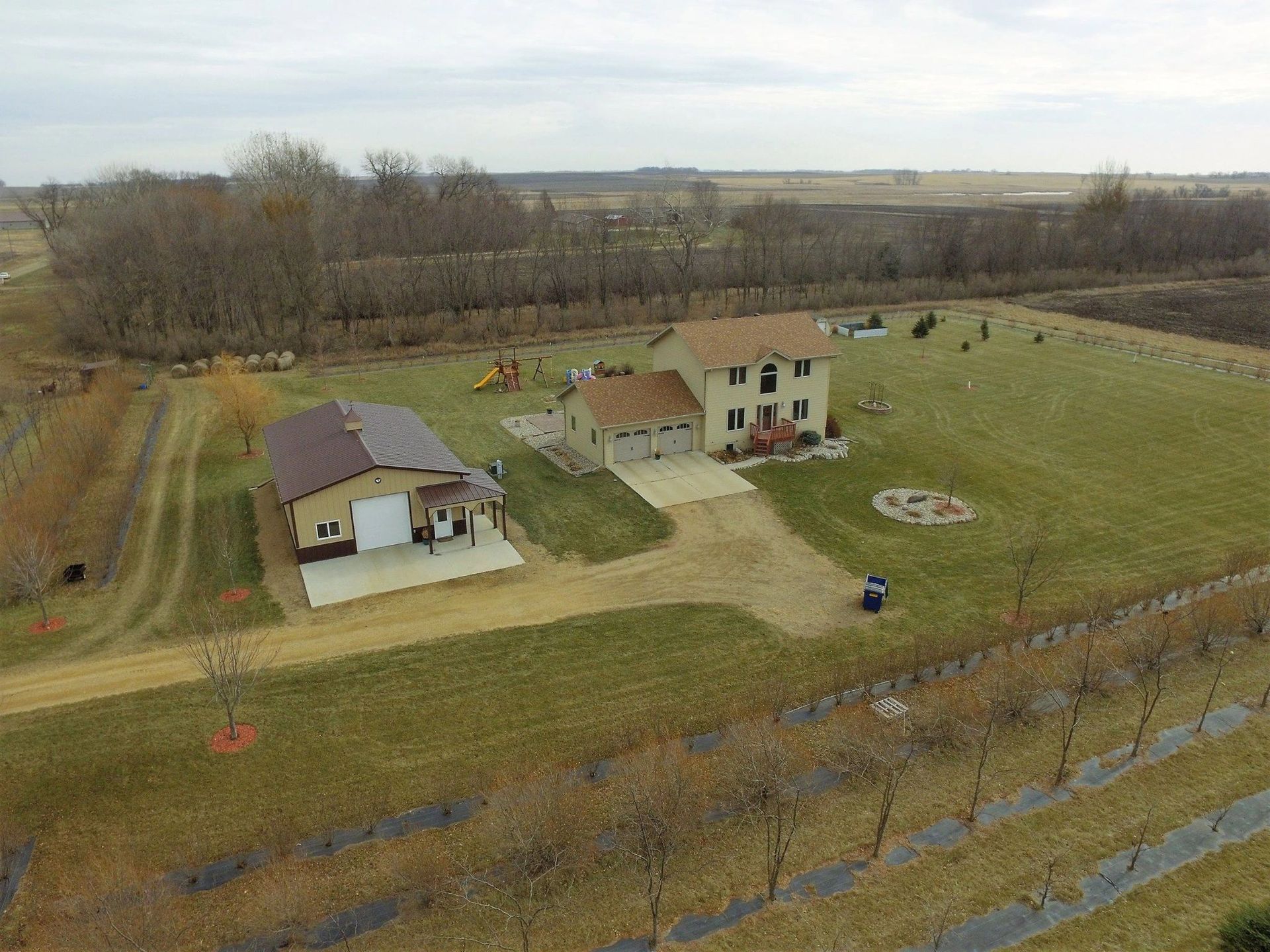 Aerial view of a beige house with a detached brown garage, both on a grassy lot.