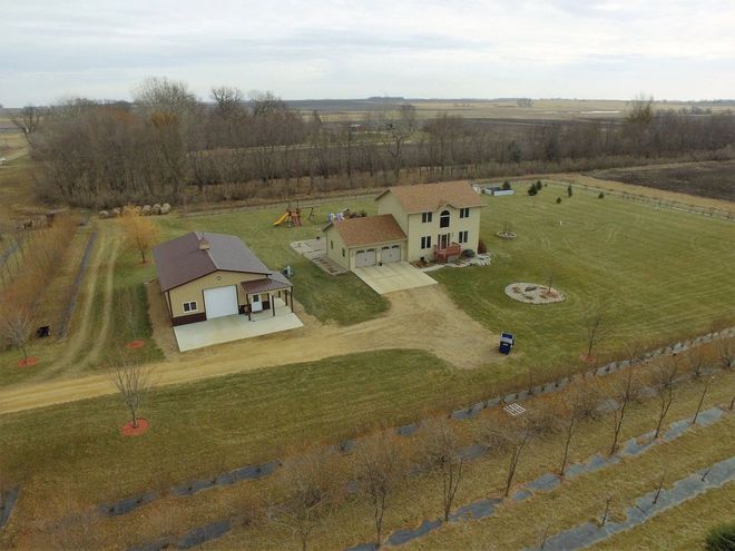 Aerial view of a beige house with a detached garage on a grassy lot, trees in the background.