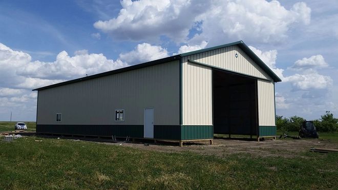 Large metal barn with open front in a field. Green and cream exterior, blue sky.