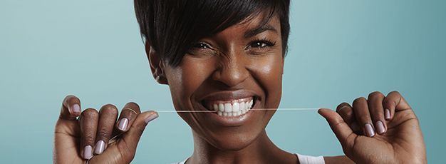 Smiling person holding a string of white dental floss against a blue background