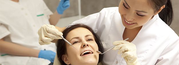 Dentist examining a smiling patient in a dental clinic, with a nurse assisting nearby.