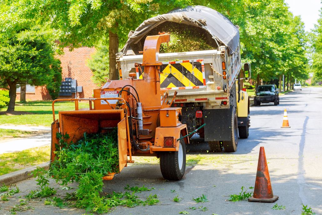 Street tree-trimming truck with orange chipper and cones on a residential road