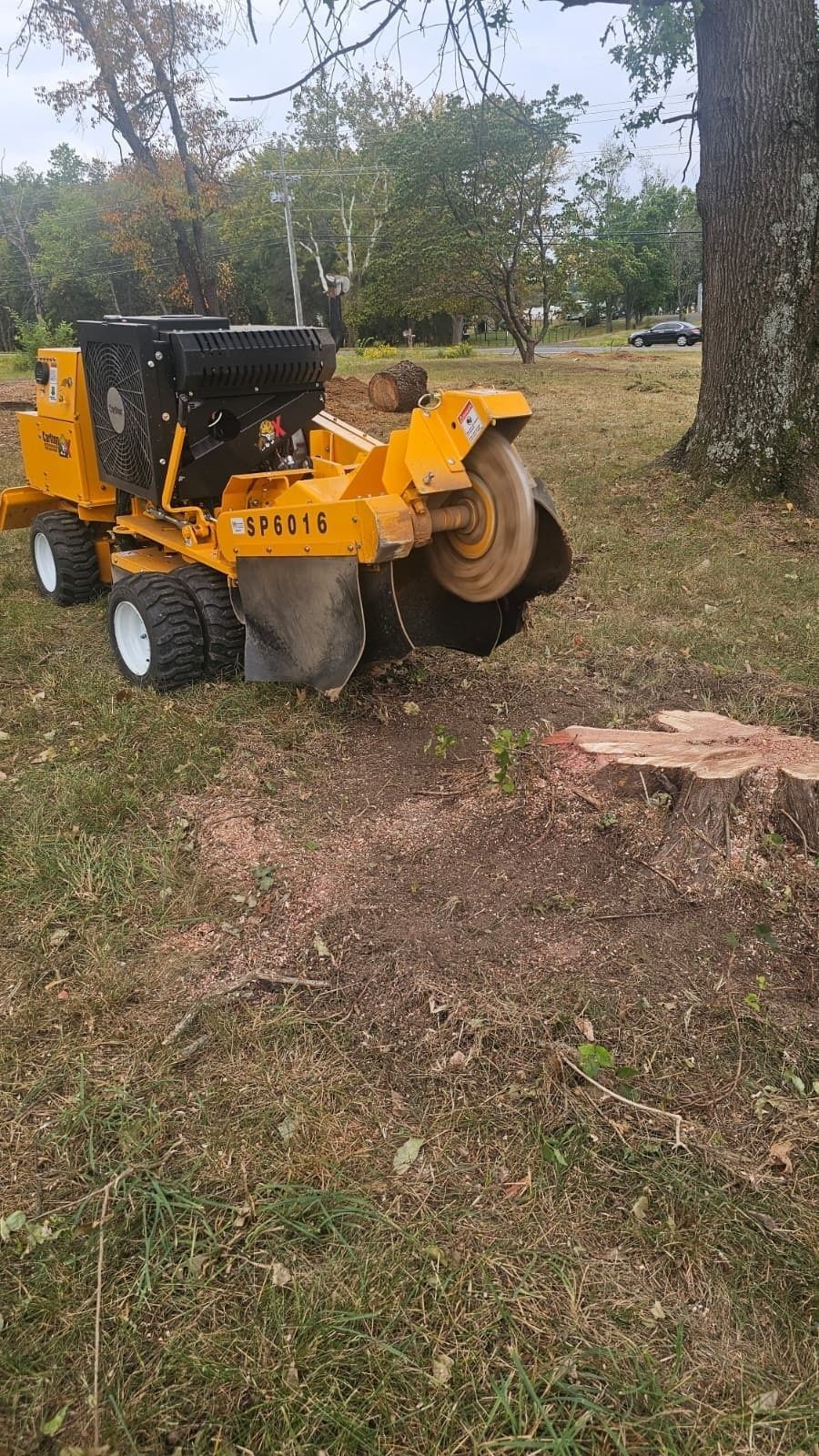Orange wood chipper parked on grass near a tree in a yard, with a pickup truck in the background