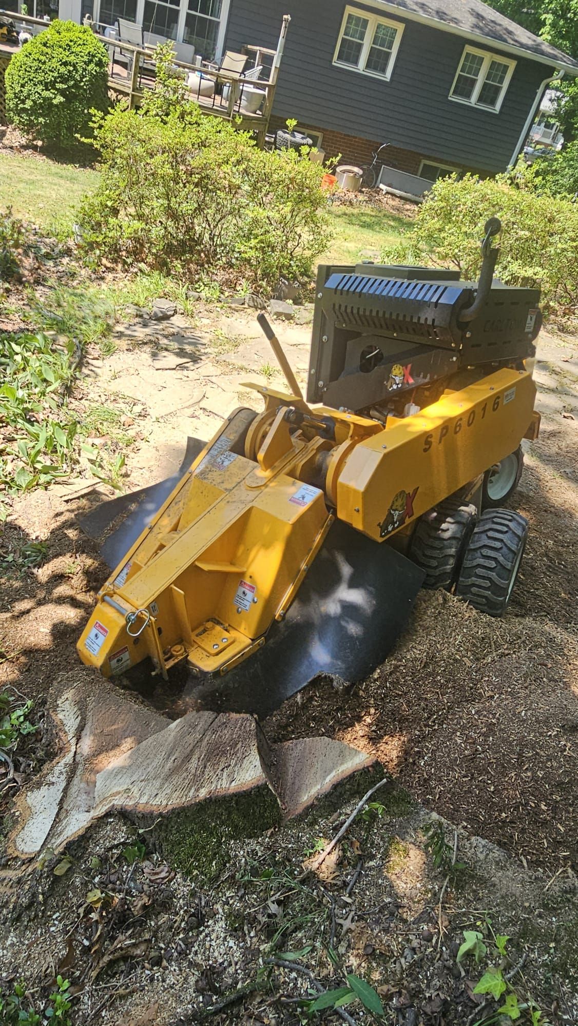 Yellow construction loader digging in a rocky garden beside a house