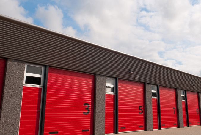 A row of red garage doors on a building with a blue sky in the background.
