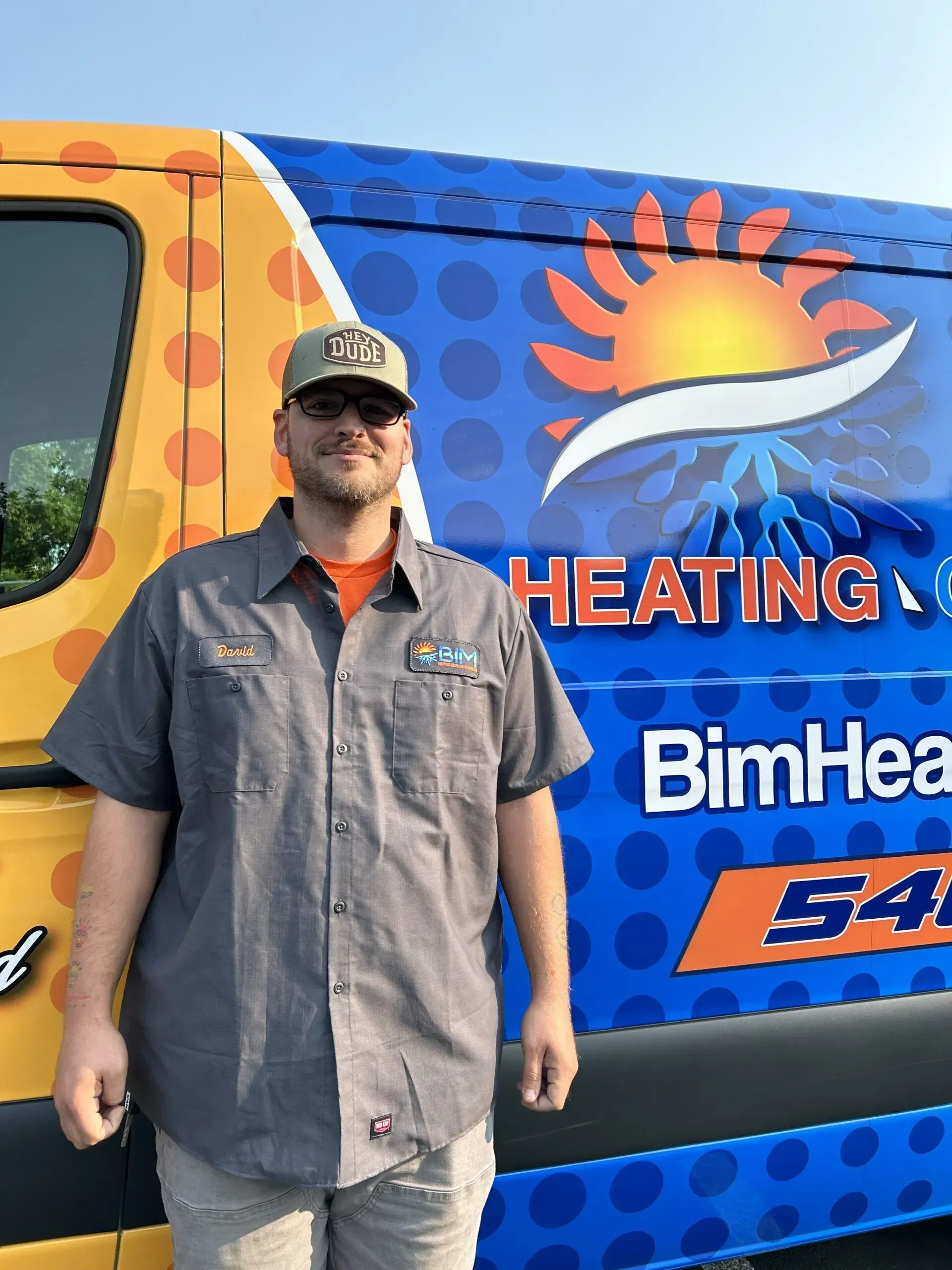 Man standing beside a blue-and-orange heating service van with sun logo and company branding