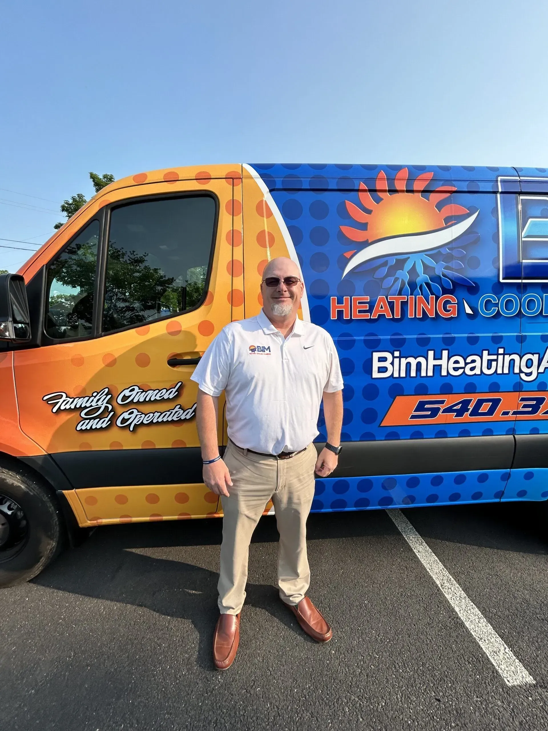 Man standing beside an orange-and-blue Heating & Cooling service van in a parking lot