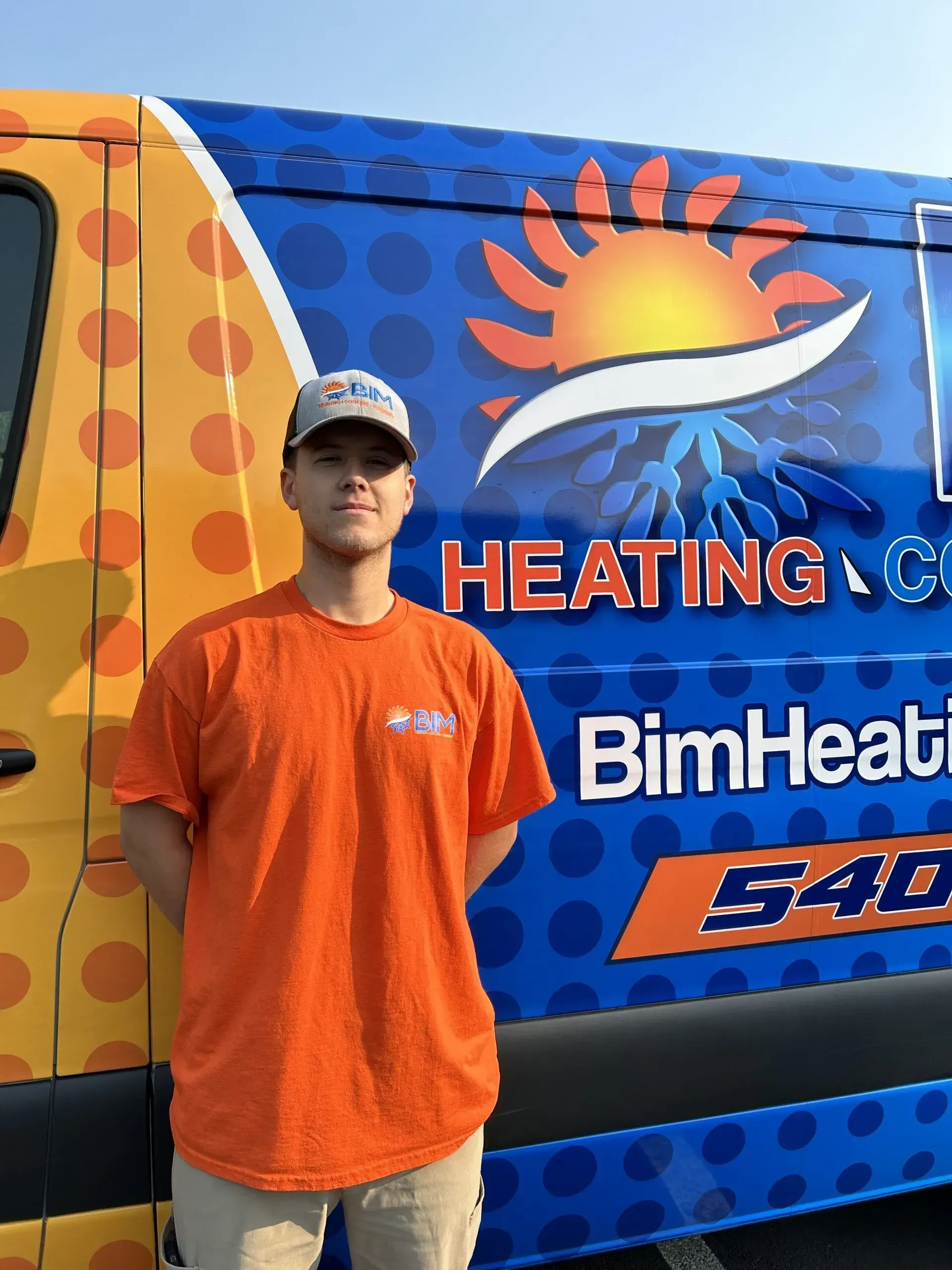 Man in orange shirt standing beside a colorful heating company truck with sun logo