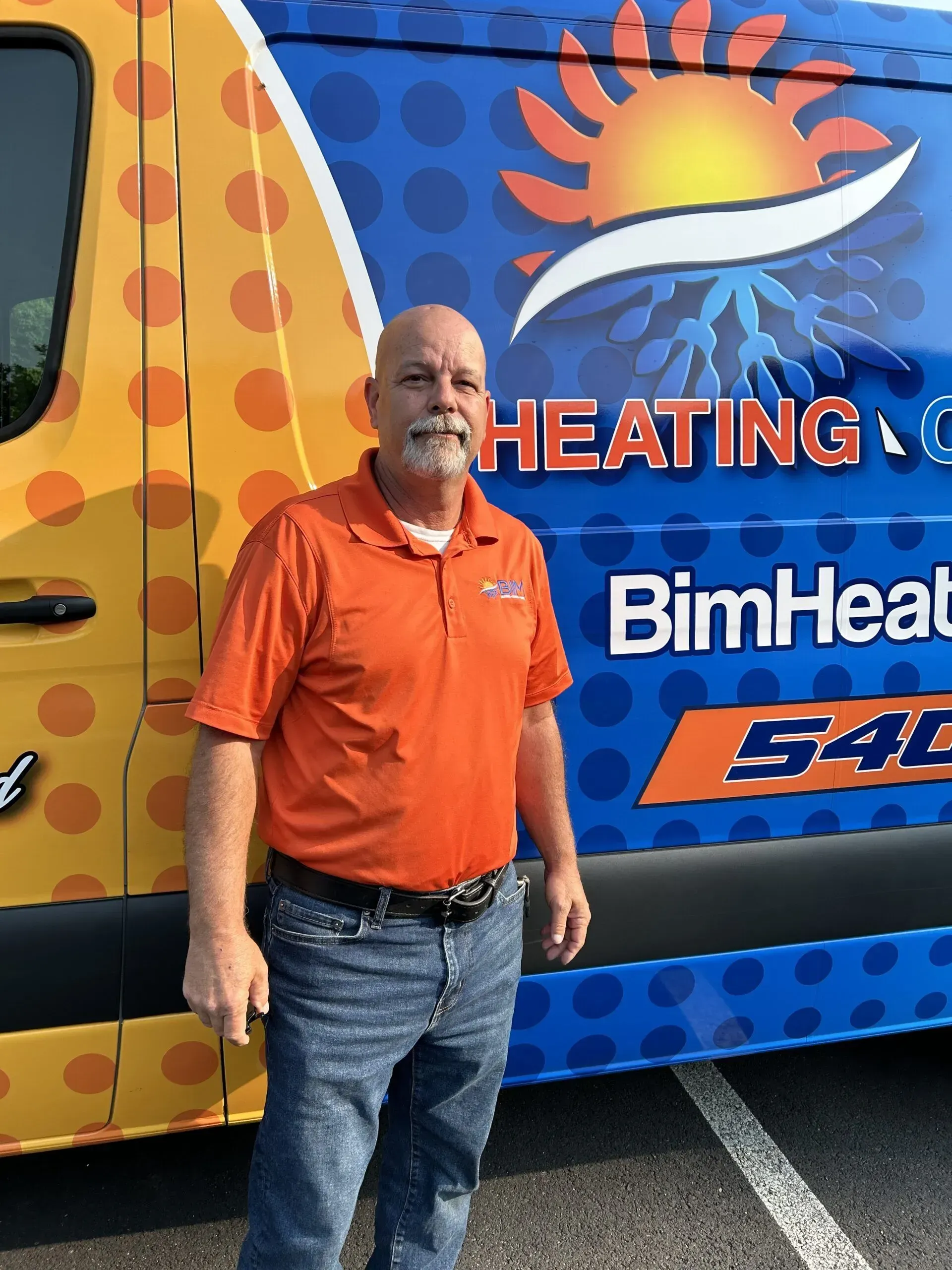 Man in orange polo standing beside a colorful heating service van with sun logo and “HEATING” text