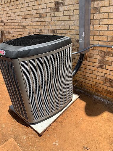 Outdoor air conditioner unit beside a brick wall on a concrete pad