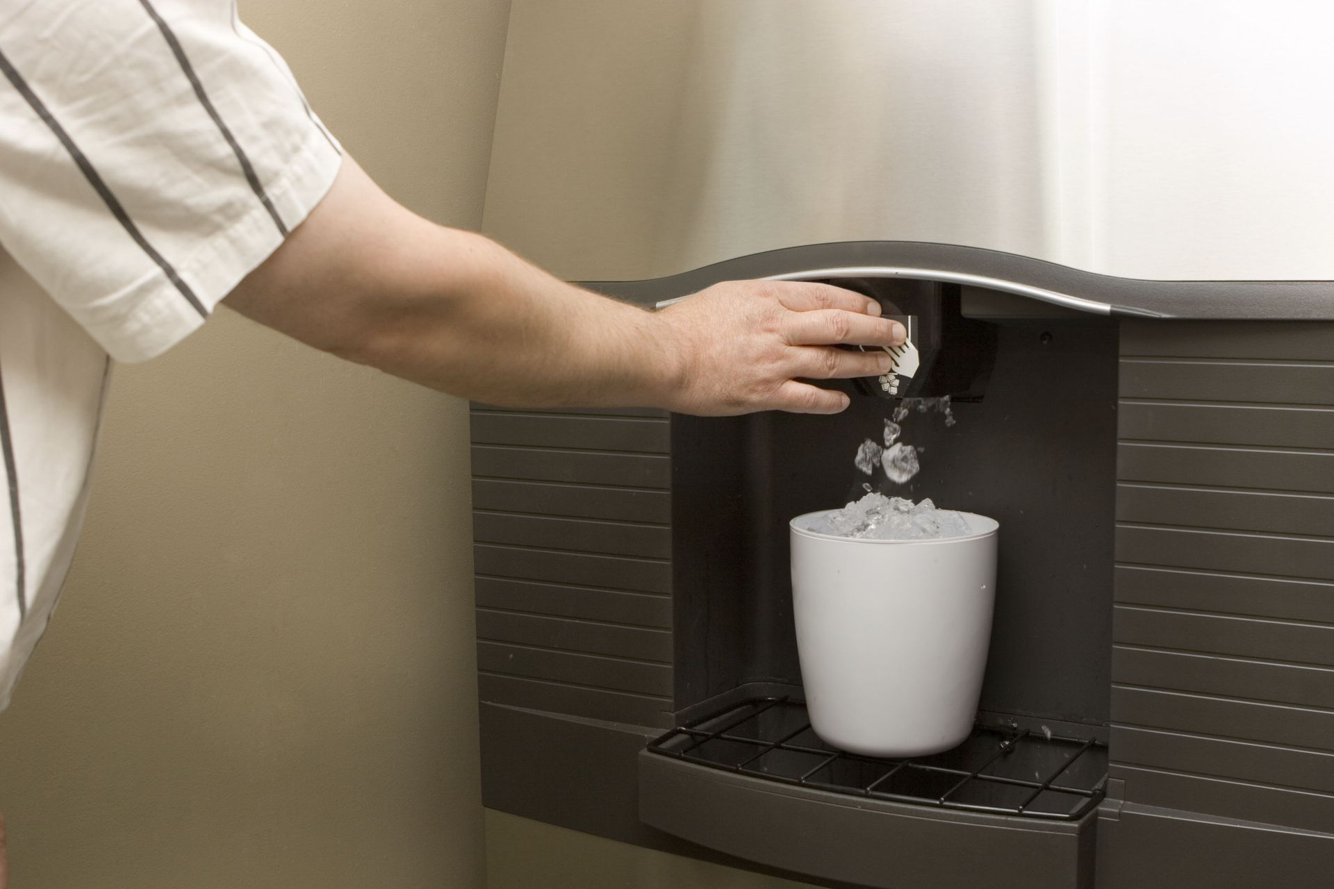 Person dispensing ice cubes from a commercial ice machine into a white cup.