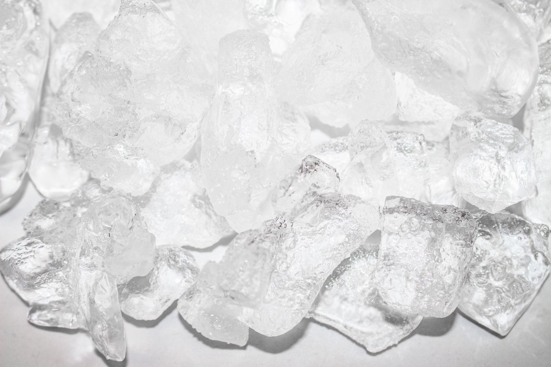 Pile of clear, irregularly shaped ice cubes, reflecting light and glistening.