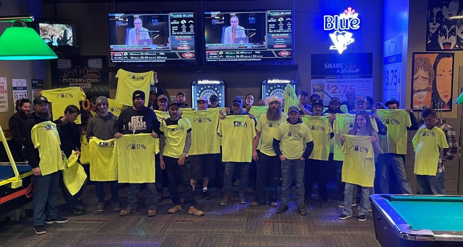 A group of people standing in front of a pool table holding yellow shirts.