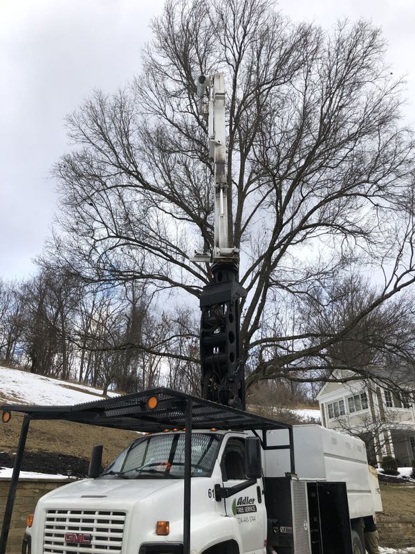 A white truck with a crane on top of it is parked in front of a tree.
