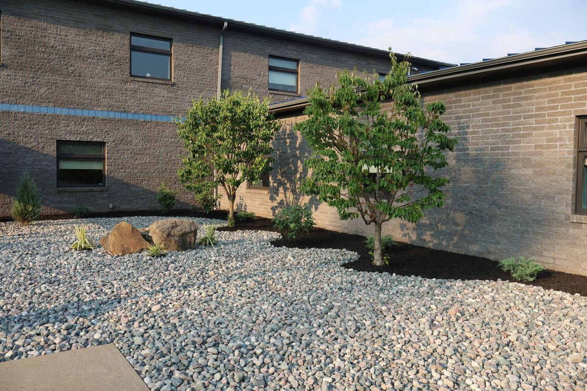 Exterior of brick building with small trees and rock landscaping.