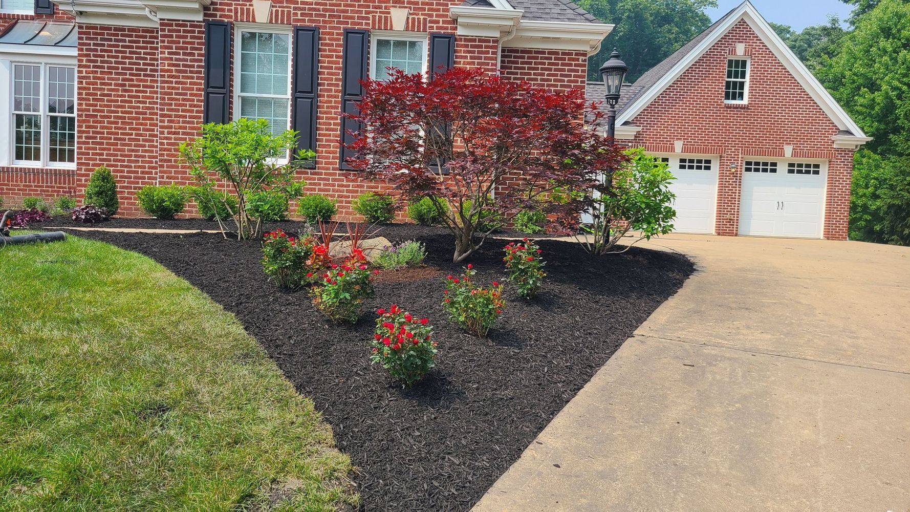 A brick house with a driveway and a lot of flowers in front of it.