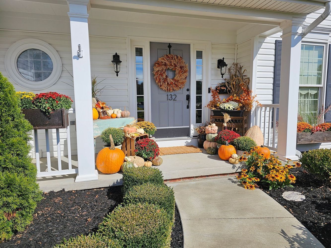 A white house with a porch decorated for fall with pumpkins and flowers.
