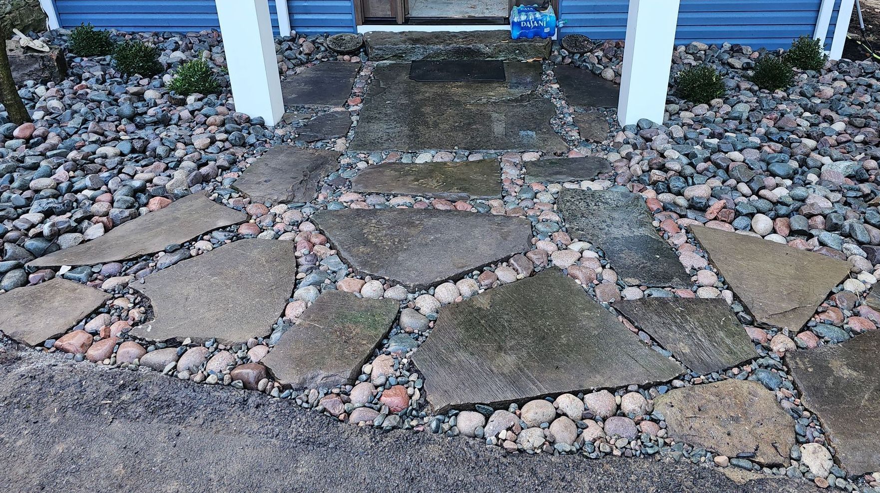A stone walkway is surrounded by rocks in front of a blue house.