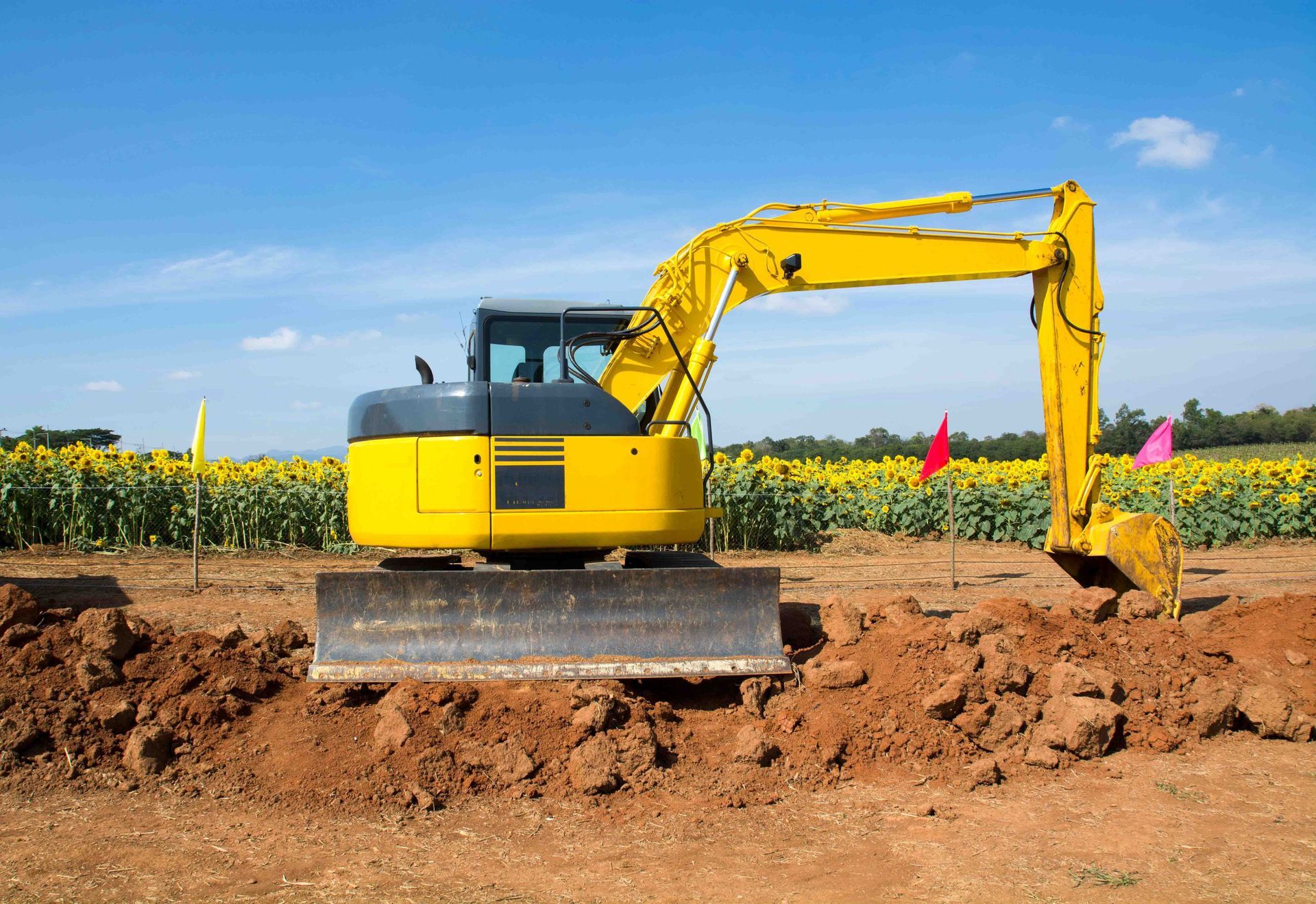 Yellow excavator digging in brown dirt under a blue sky.
