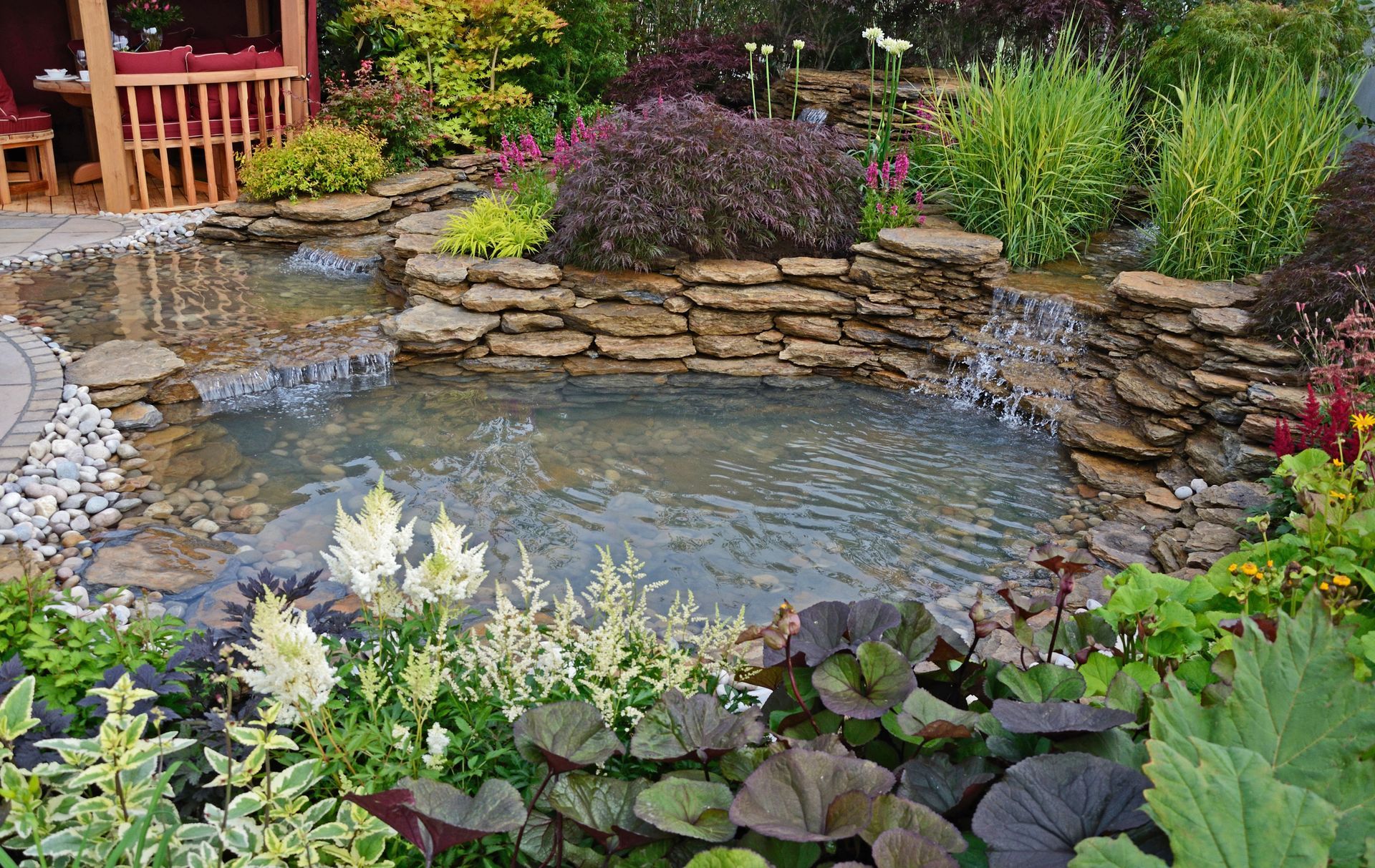 Pond with layered stonework, small waterfalls, and surrounding lush, colorful flowers.