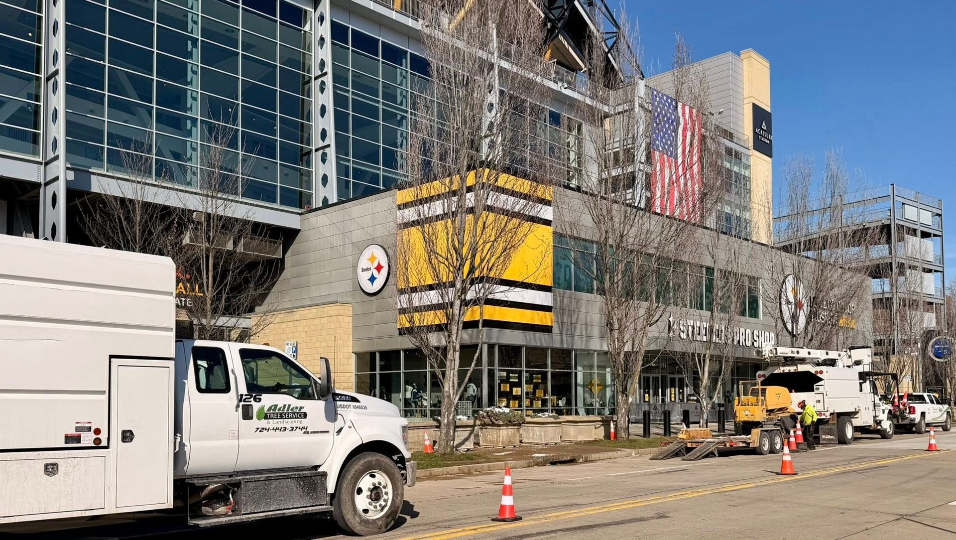 Construction vehicles parked outside a building displaying a yellow Pittsburgh Steelers banner and an American flag.