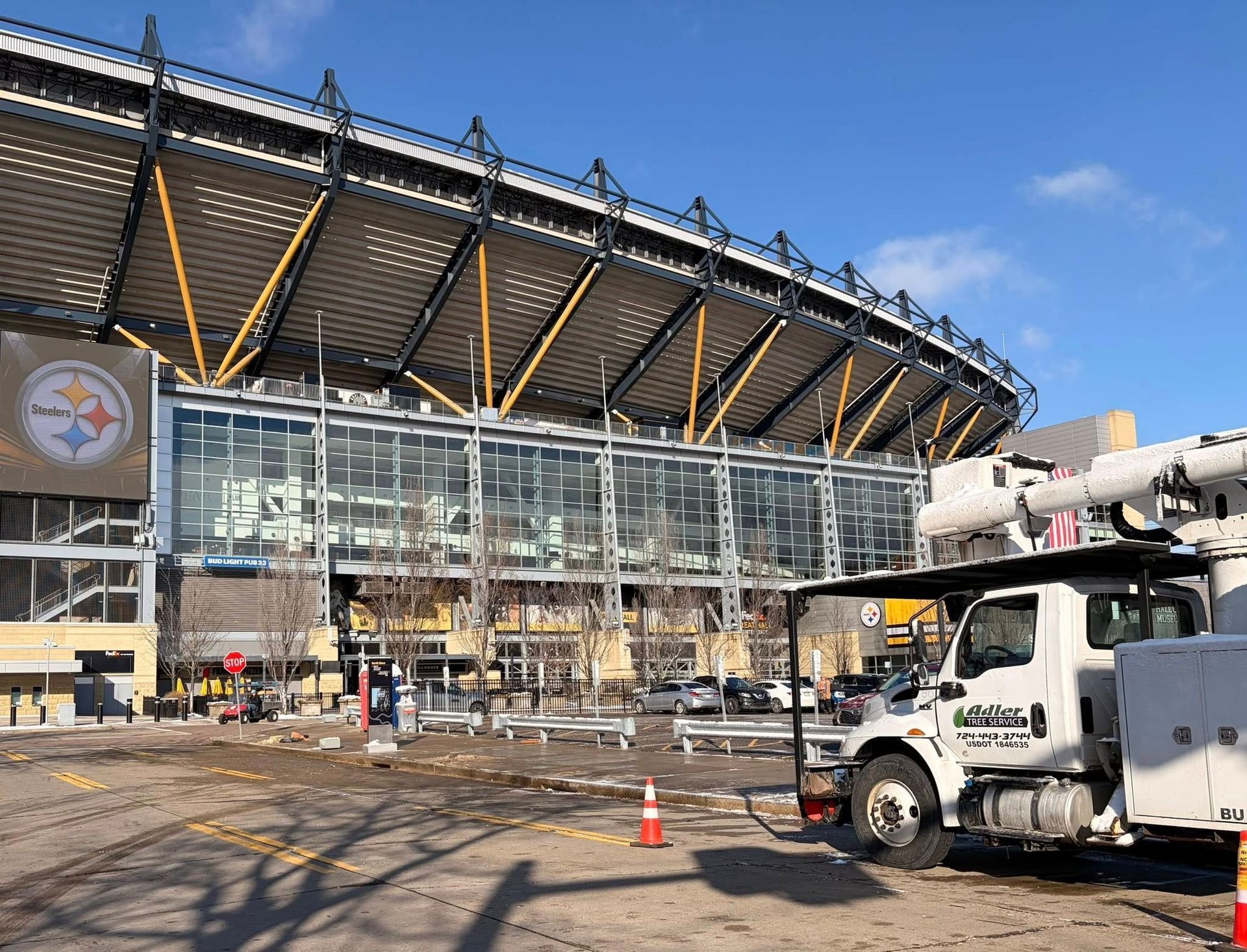 Exterior view of Acrisure Stadium in Pittsburgh with a white utility truck parked in the foreground on a sunny day.