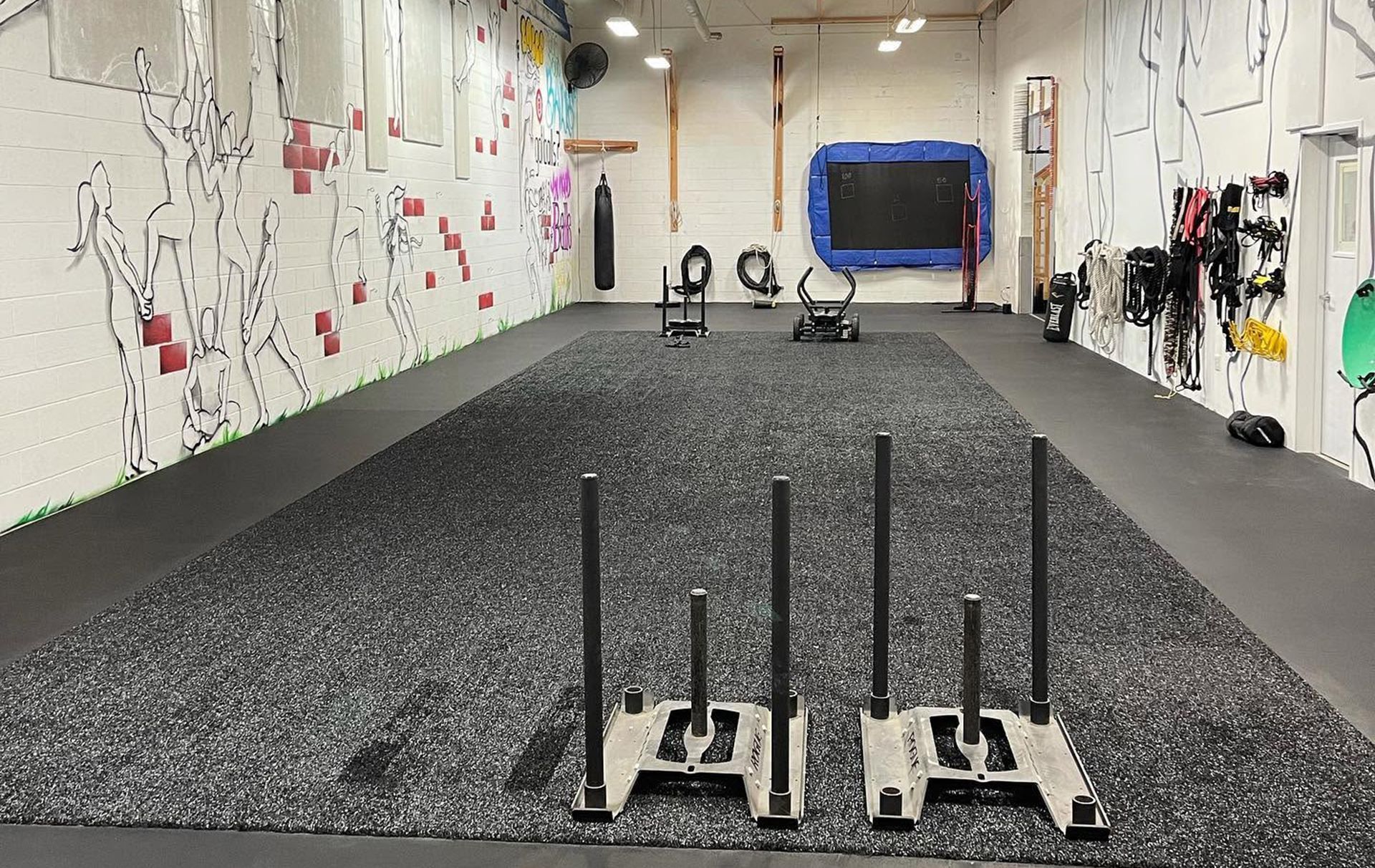 Indoor training gym with sleds on a black turf lane and exercise equipment along the walls