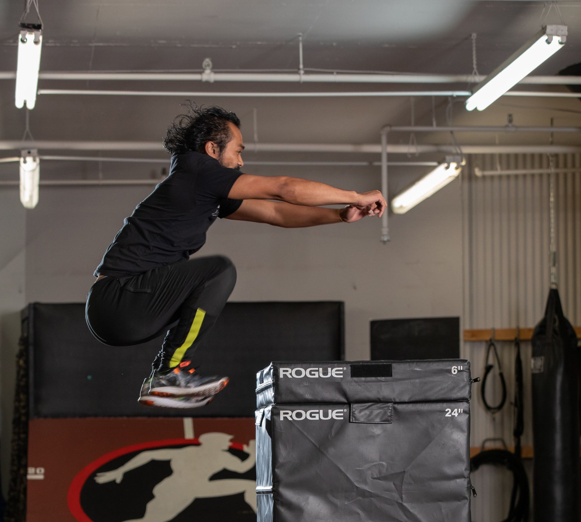 Athlete mid-jump on a gym box, arms extended forward during a plyometric exercise