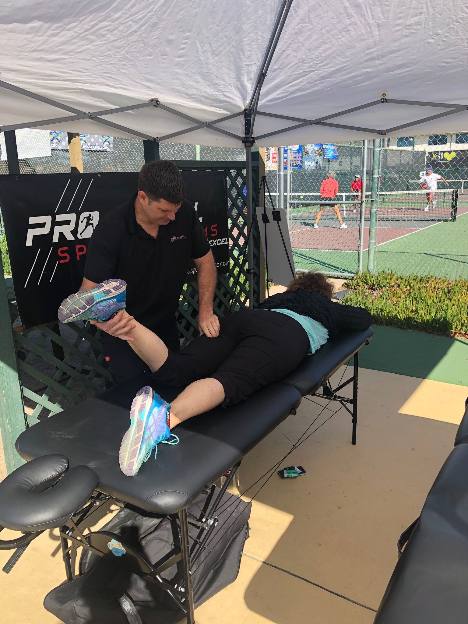 Athlete receiving leg massage on a treatment table under a tent at an outdoor sports field