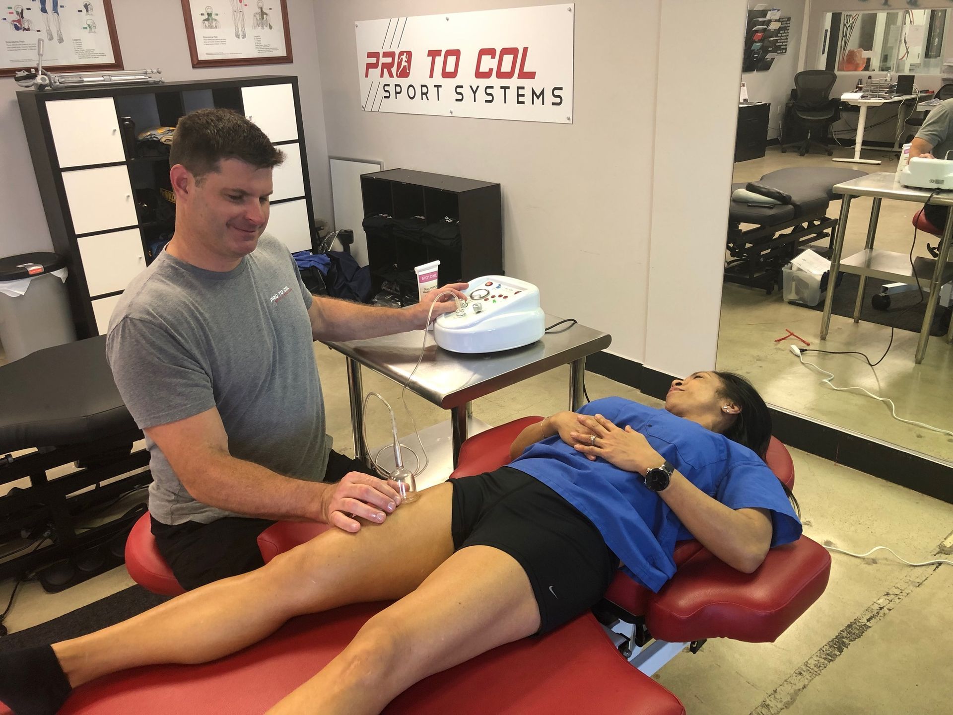 Person receiving treatment on a red therapy table while a clinician monitors a device in a sports medicine clinic