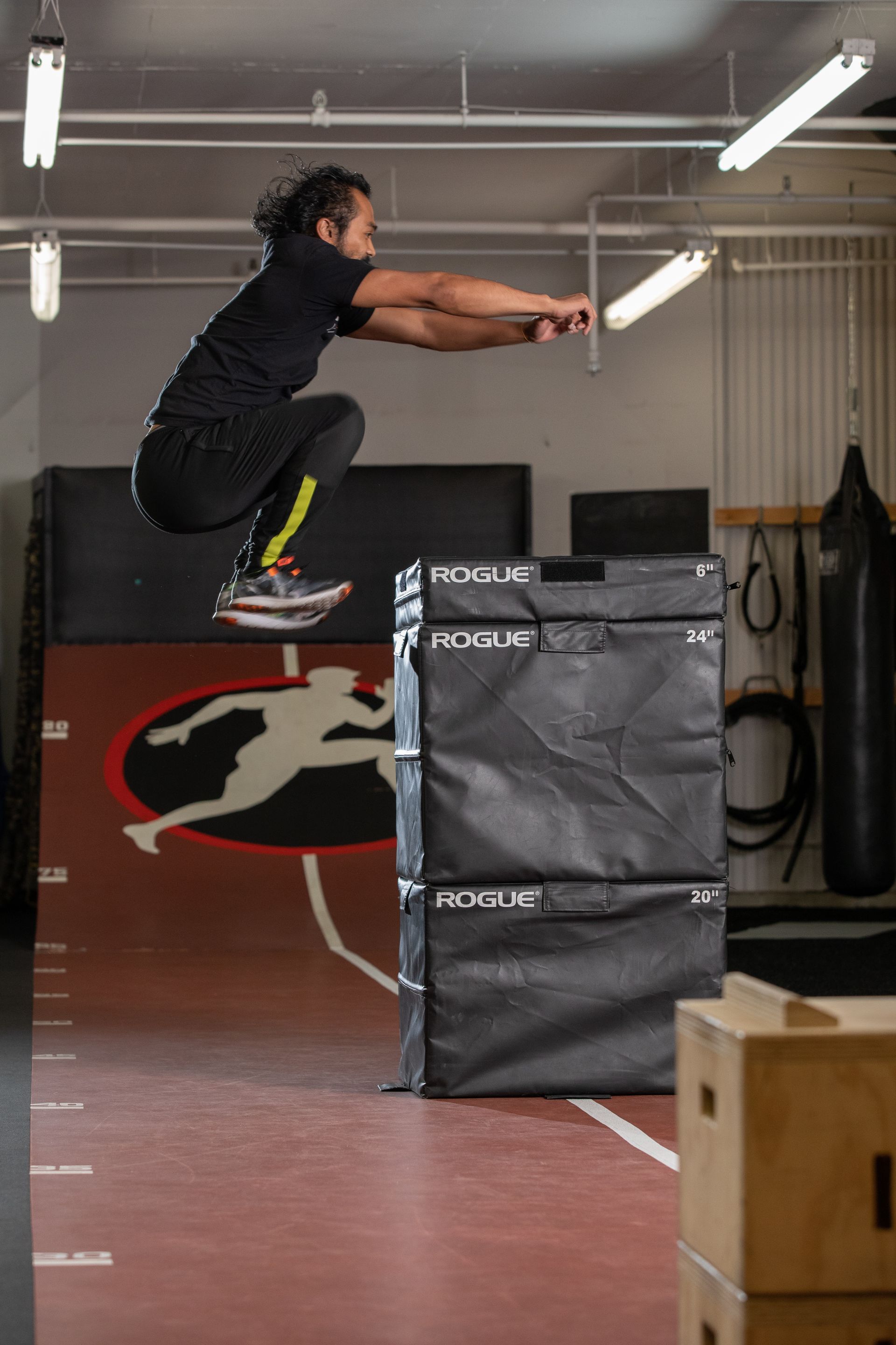 Athlete mid-jump over stacked boxes in an indoor gym, arms extended forward.