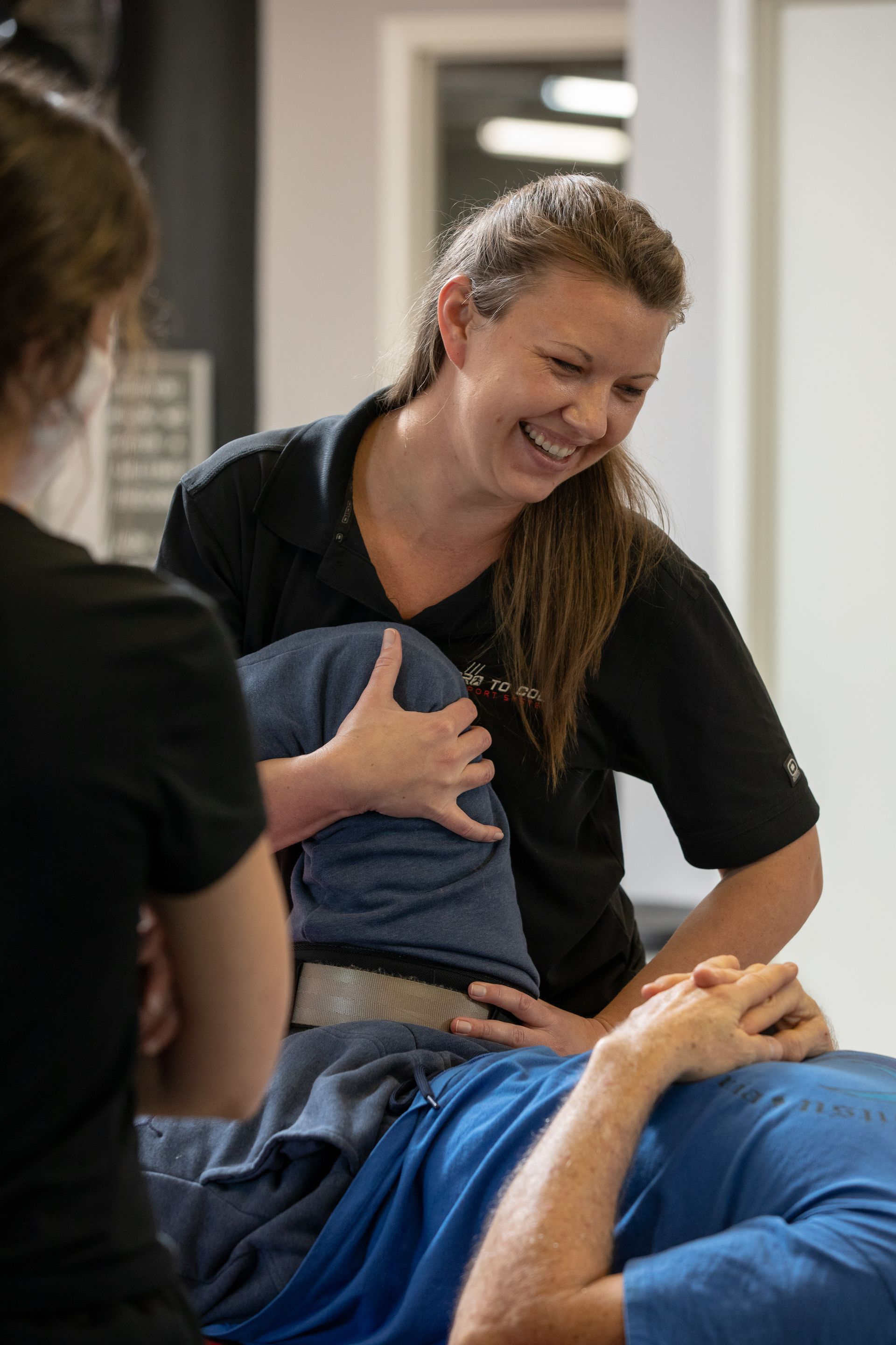 Therapist in black shirt assists a reclining patient during a hands-on treatment session
