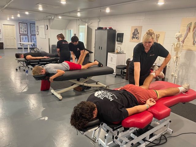Several people receiving massage therapy on tables in a bright clinic room