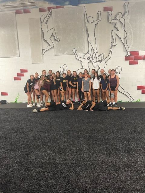 Group of people posing in a gym in front of a mural wall and black turf flooring