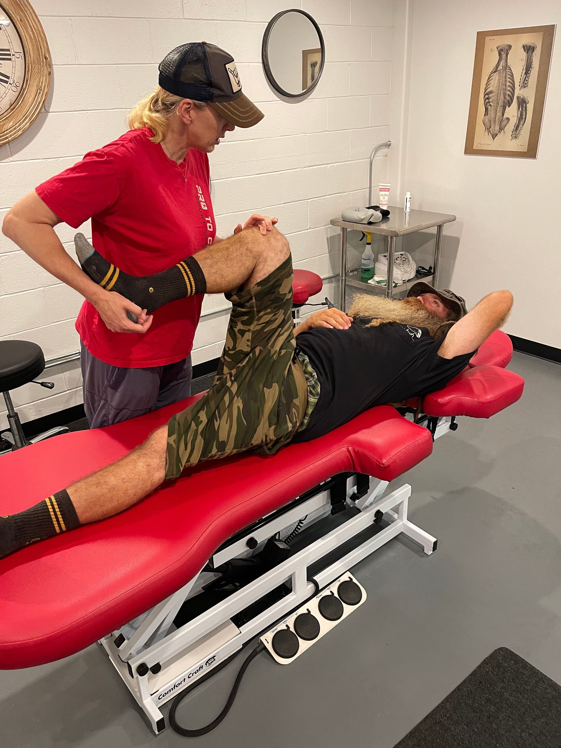 Therapist stretching a patient’s leg on a red treatment table in a clinic room