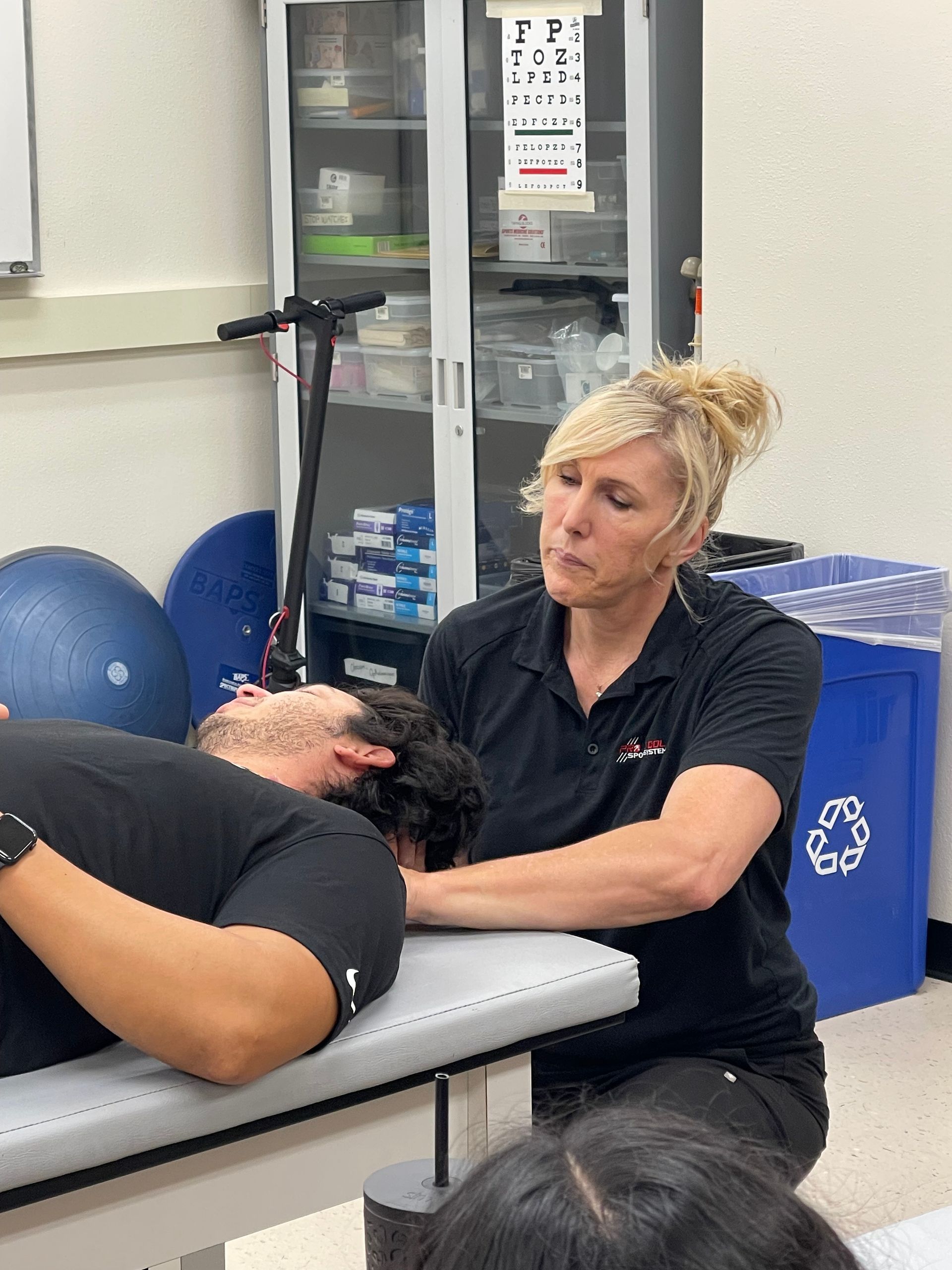 Massage therapist treating a patient on a table in a clinic, with exercise balls and a cabinet in the background