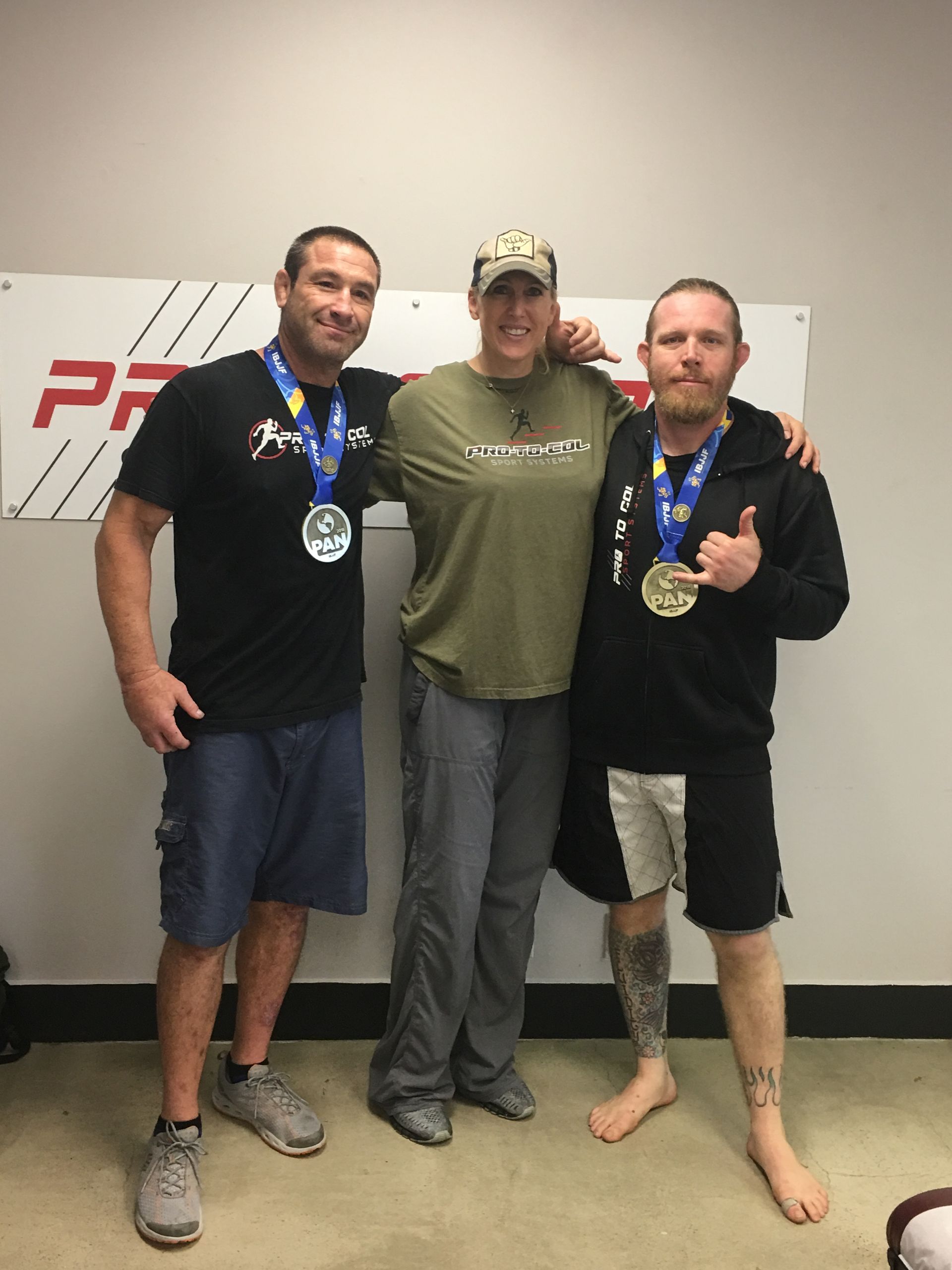 Three people posing indoors with medals around their necks, standing in front of a banner.