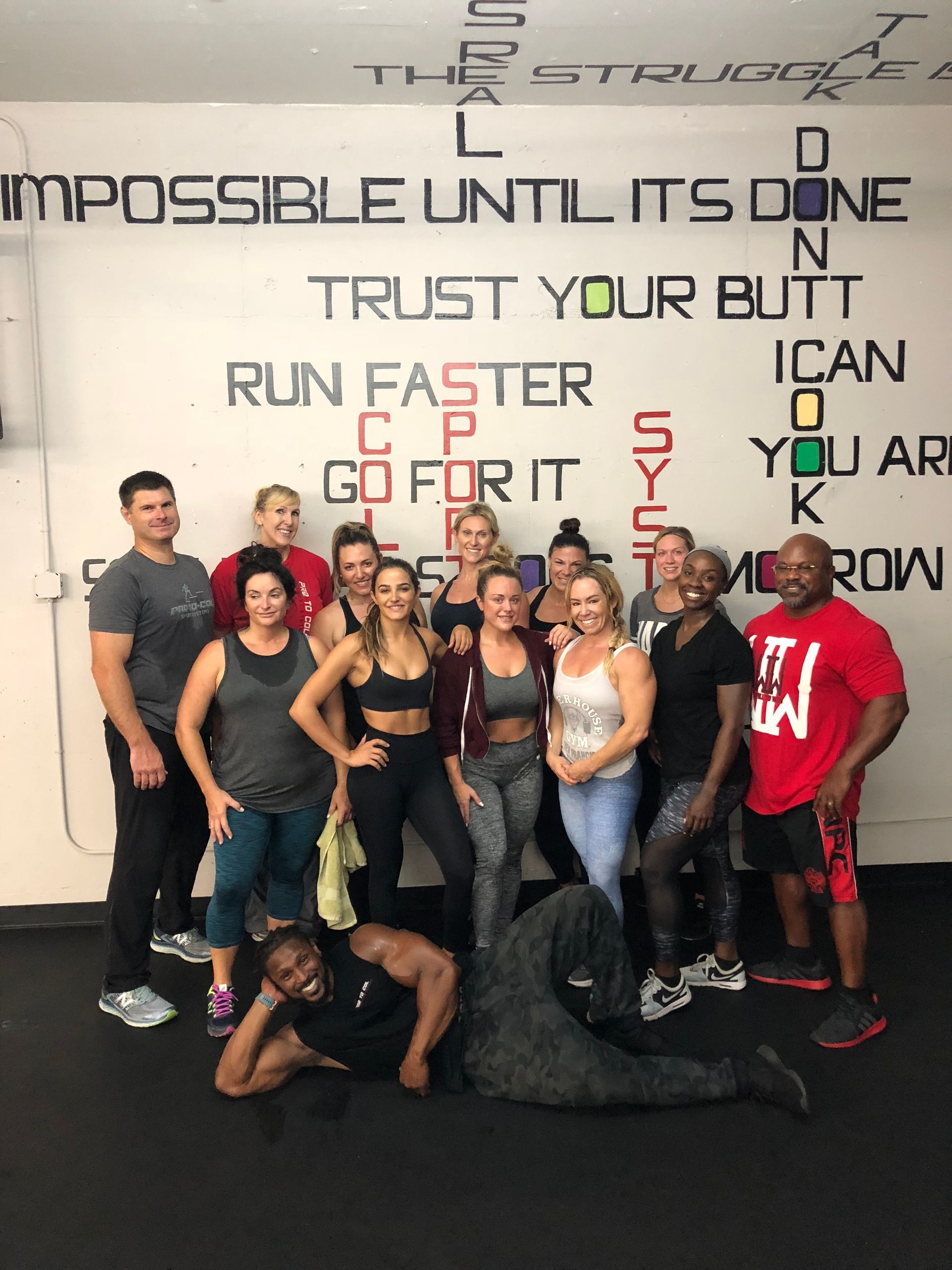 Group of people posing in a gym in front of an “Impossible until it’s done” motivational wall sign.