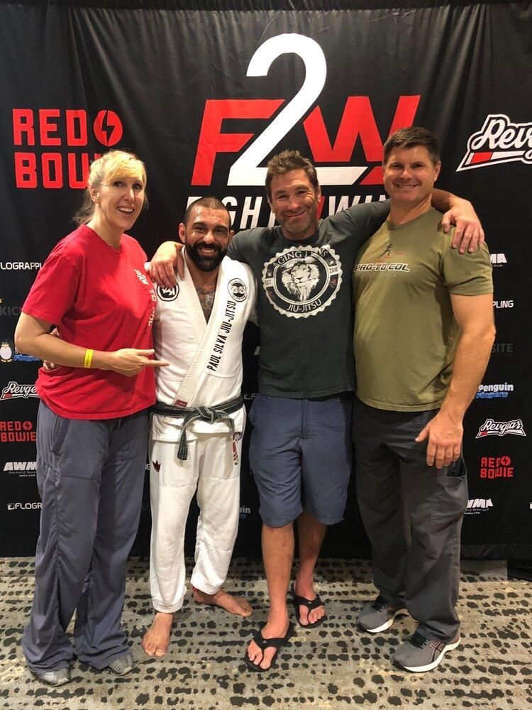 Four people posing together at a jiu-jitsu event in front of a Red Zone backdrop.