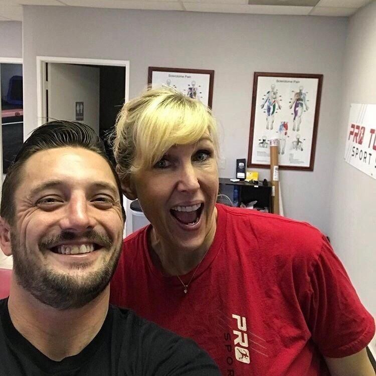 Two smiling people taking a selfie in an office, one wearing a red shirt.