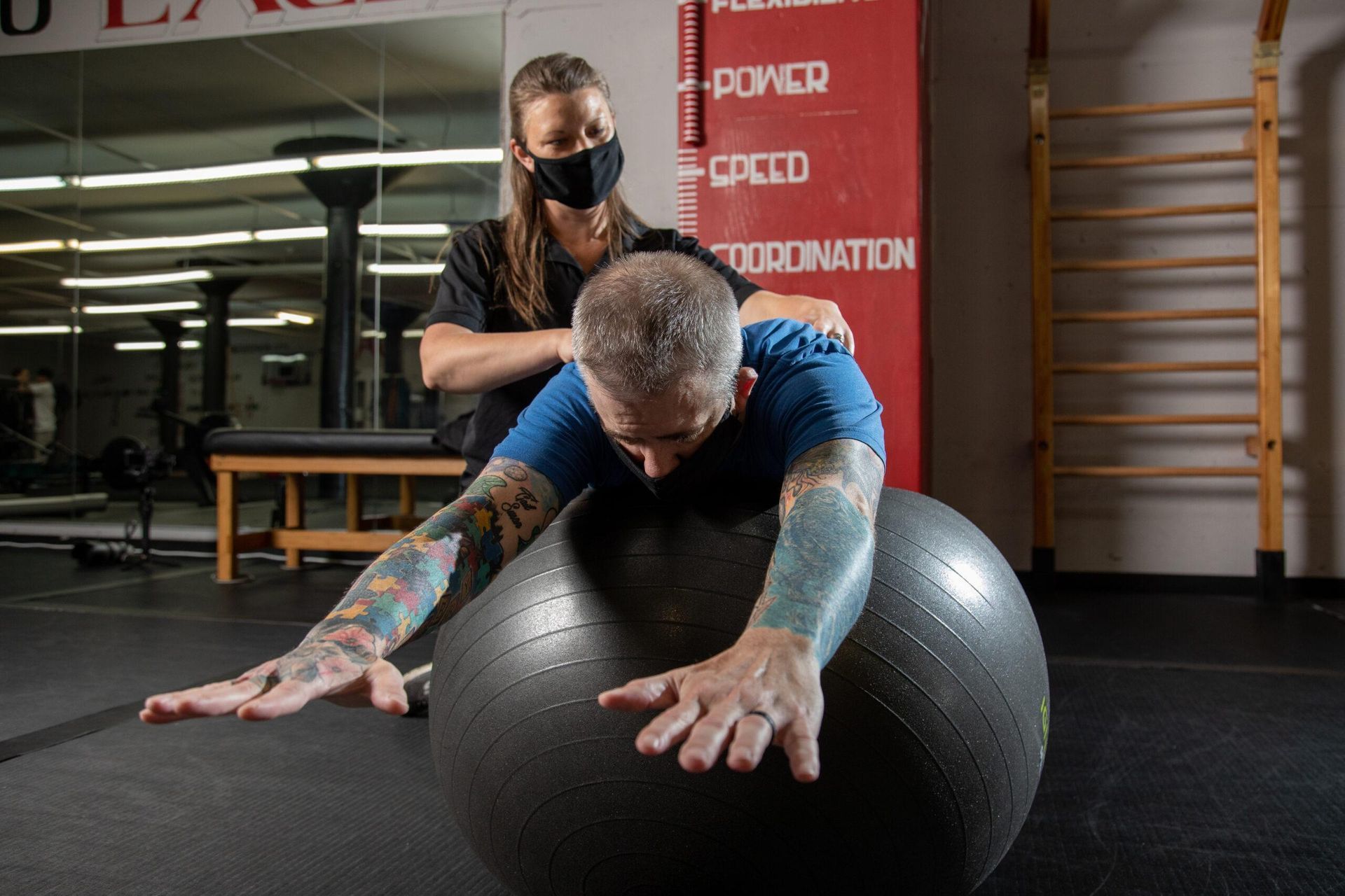 Trainer assists athlete rolling on a large exercise ball in a gym